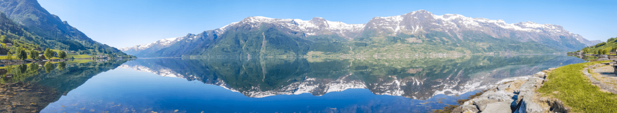 Mächtige, schneebedeckte Felsen spiegeln sich im kristallklaren Wasser des Eidfjords in Norwegen.