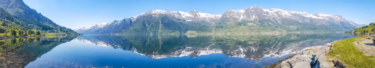 Mächtige, schneebedeckte Felsen spiegeln sich im kristallklaren Wasser des Eidfjords in Norwegen.
