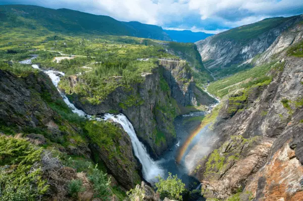 Voringsfossen Der malerische Wasserfall Voringsfossen stürzt sich inmitten einer üppig grünen Landschaft in die Tiefe. Auf der rechten Seite hat sich ein Regenbogen gebildet.
