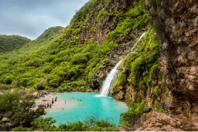 Ein kleiner türkisfarbener Naturwasser-Pool in welchen das Wasser des AYN Khor Wasserfalls fließt. Dieser liegt inmitten von Felsen und Wald