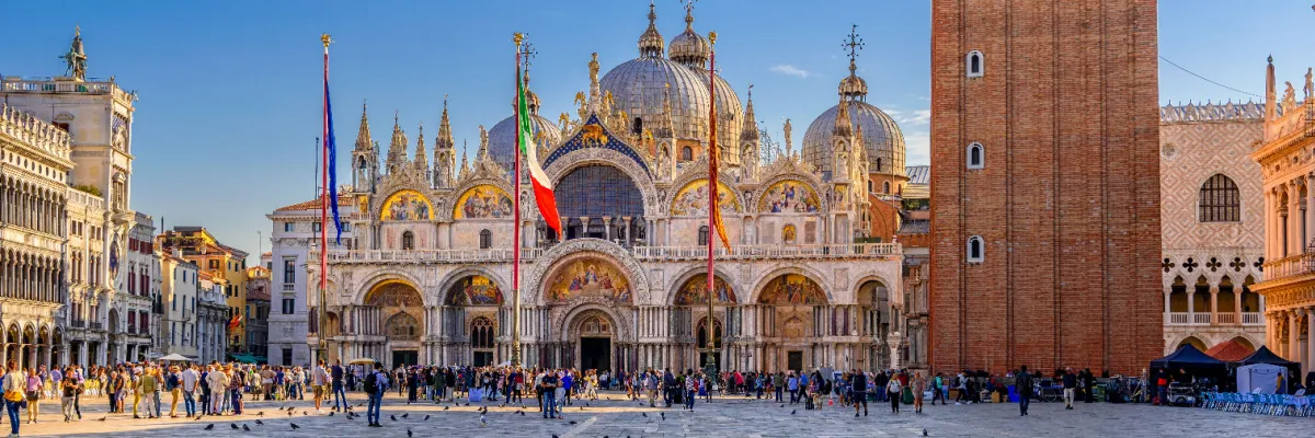 Der prächtige Markusdom mit seinen goldenen byzantinischen Kuppeln und Mosaiken an der belebten Piazza San Marco in Venedig bei strahlendem Sonnenschein.