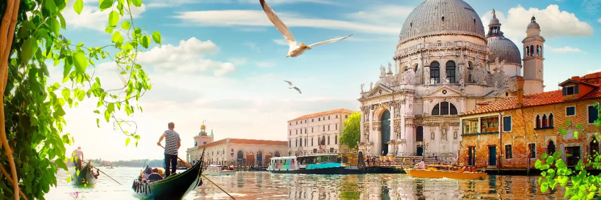 Ausblick vom Canal Grande auf die herrschaftliche Kirche Santa Maria della Salute und vorbeigleitende Gondeln während eines Landausflugs.