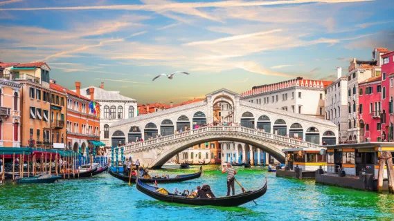 Traditionelle Gondeln auf dem smaragdgrünen Canal Grande vor der historischen Rialtobrücke in Venedig bei sanftem Abendlicht.