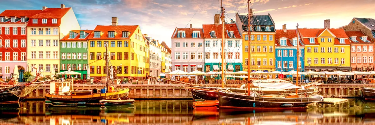 Die berühmten bunten Häuserfassaden des Nyhavn in Kopenhagen mit historischen Segelschiffen und Spiegelungen im Wasser bei klarem Himmel.