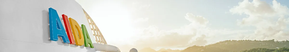 Der AIDA-Schriftzug an der Außenseite der AIDAperla morgens von goldenem Sonnenschein angestrahlt.