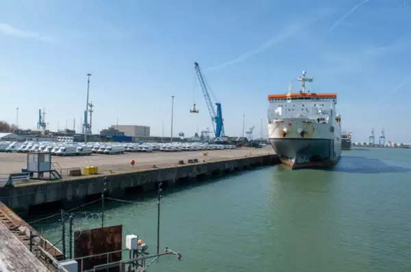 Ein Containerschiff im Hafen von Zeebrügge bei Antwerpen. Im Hintergrund sind Kräne beim Verladen von Containern zu sehen.