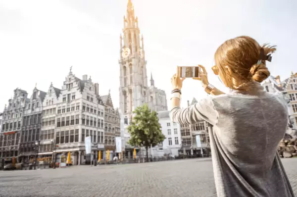 Eine junge Frau fotografiert am Grote Markt die Liebfrauenkathedrale und die Zunfthäuser mit ihrem Smartphone.