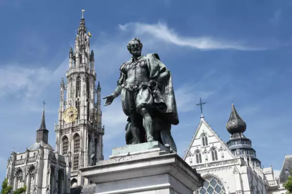 Eine Statue des Malers Peter Paul Rubens vor der Liebfrauenkathedrale in Antwerpen. Links ist der filigrane Turm, rechts ein Querschiff der Kirche zu sehen.