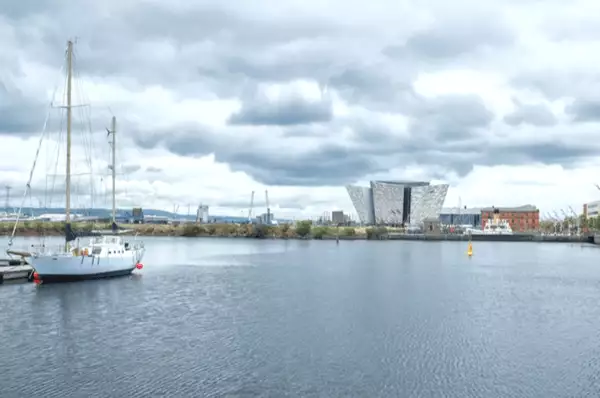 Im Vordergrund ist ein Segelboot und im Hintergrund das Titanic Museum in Belfast zu sehen