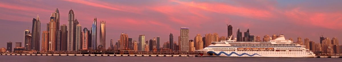 Die Skylune von Dubai im Sonnenuntergang mit einem Kreuzfahrtschiff im Vordergrund.