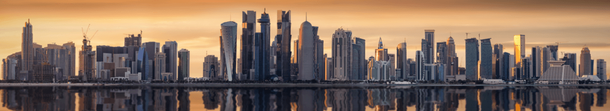 Die Wolkenkratzer von Doha in gelblichen Licht eines bewölkten Sonnenuntergangs.