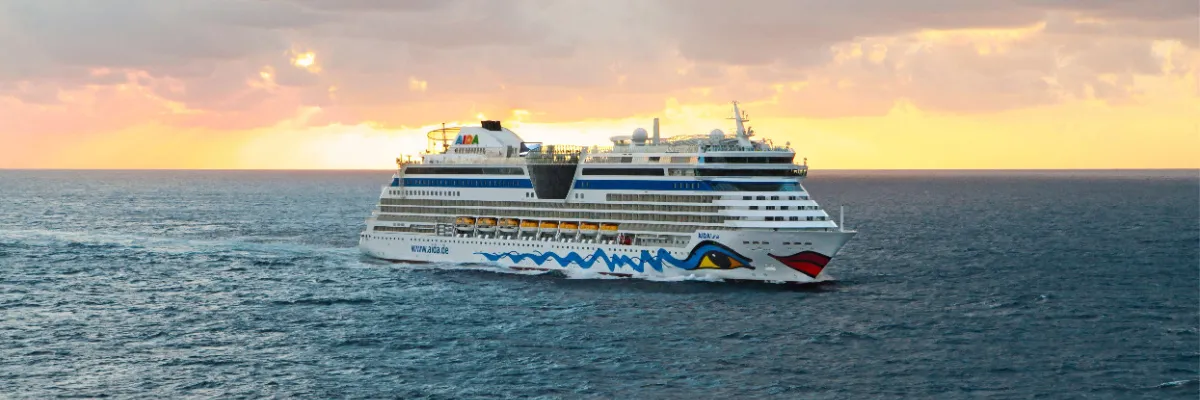 Ein AIDA Schiff kreuzt während der goldenen Stunde bei einem spektakulären Sonnenuntergang auf dem offenen Meer. Die Aufnahme fängt die weite Sicht und die maritime Ruhe einer spontanen Last Minute Reise ein.