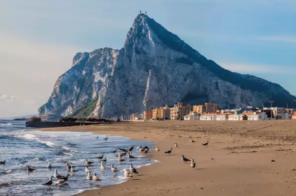 Blick auf den Felsen von Gibraltar vom Strand aus Blick auf den Felsen von Gibraltar vom Strand aus mit vielen Möwen am Strand und leichten Wellen des Meeres