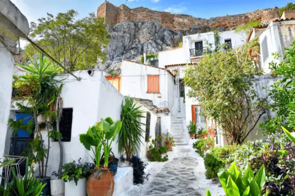Strahlend weiße Häuser an einer malerischen, mit vielen Pflanzen geschmückten Gasse im Athener Stadtteil Anafiotika. Im Hintergrund der Burgberg mit der Akropolis.