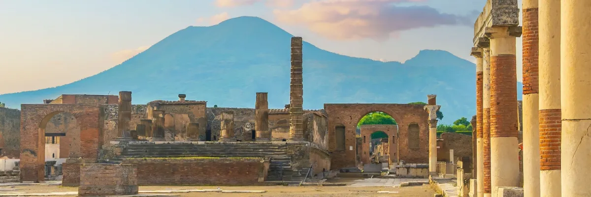 Antike Säulen und Ruinen in Pompeji mit dem Vulkan Vesuv im Hintergrund bei Sonnenuntergang.