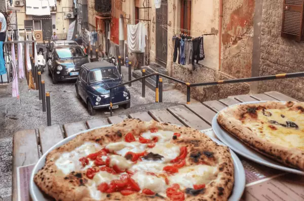 Typisch Neapel: Schmale Gassen & leckere Pizza Ein Tisch mit zwei Pizzen in einer schmalen Gasse in der Altstadt von Neapel.