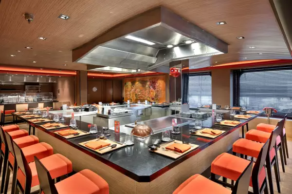 Kaito Teppanyaki Restaurant Blick in das japanische Restaurant auf MSC Euribia mit Live-Cooking-Stationen, um die die Stühle für die Gäste aufgestellt sind.