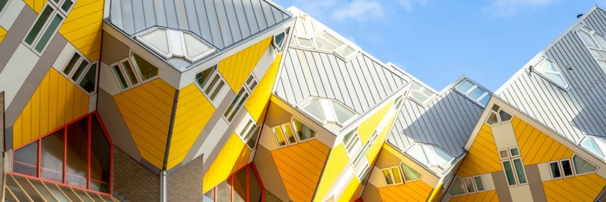 Gelben Kubushäuser in Rotterdam bei Sonnenschein. Die Häuser sind quadratisch und greifen ineinander.