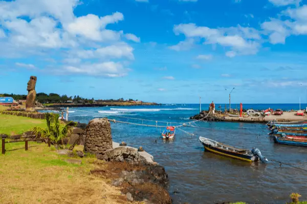 Fischerhafen in Hanga Roa mit einer Steinskulptur und blauem Meer mit einem kleinen Boot im Hintergrund auf der Osterinsel in Chile