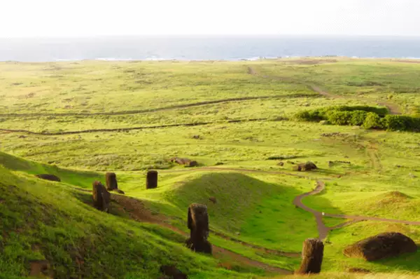 Vulkan-Wanderweg auf der Osterinsel mit zahlreichen Moai auf einer grünen Wiese im Sonnenschein