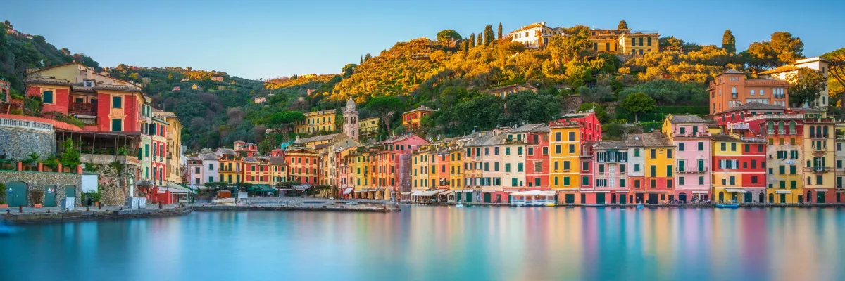 Landausflug ab Genua: Die malerische Hafenzeile von Portofino in Ligurien Panoramablick auf die bunten Häuserfronten und den ruhigen Naturhafen von Portofino an der ligurischen Küste.