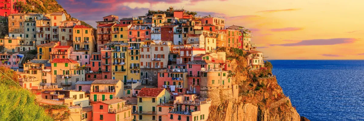 Landausflug Cinque Terre: Das spektakuläre Küstendorf Manarola in Ligurien lick auf die bunt verschachtelten Häuser von Manarola in den Cinque Terre auf einer steilen Felsklippe am Meer im warmen Abendlicht.