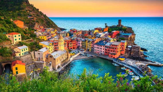 Blick auf das malerische Küstendorf Vernazza in den Cinque Terre mit bunten Häusern, dem kleinen Naturhafen und der Kirche Santa Margherita d'Antiochia bei Abendlicht.
