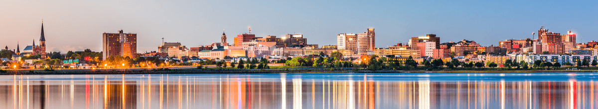 Skyline von Portland, Maine, USA bei Morgendämmerung mit leuchtenden Häusern, die sich im Wasser widerspiegeln