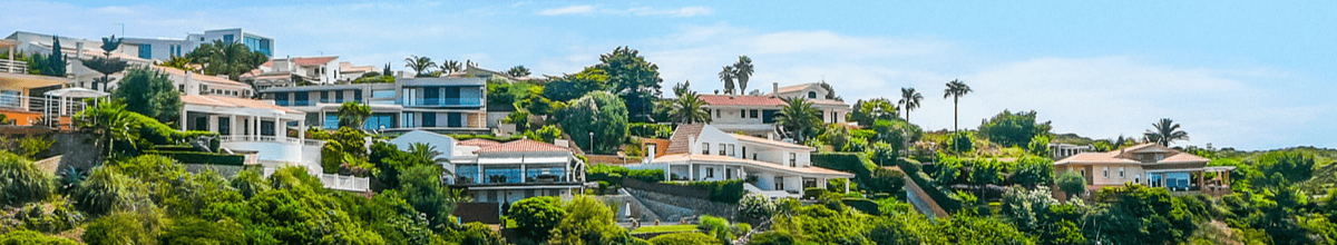 Villen an den bewaldeten und palmenbestandenen Hängen von Mahón auf Menorca.