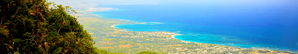 Faszinierende Aussicht auf die Stadt Puerto Plata und den tiefblauen Atlantik vom Gipfel des Pico Isabel de Torres mit tropischen Pflanzen im Vordergrund und der Stadt im Hintergrund