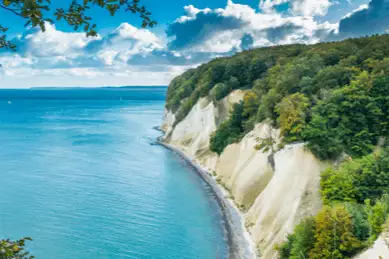 Die weißen und steilen Kreidefelsen der Insel Rügen mit blauem Meer und leicht bewölktem Himmel