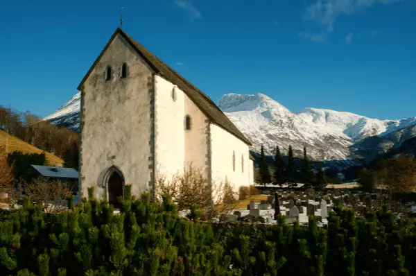 Kvinnherad Kirche in Rosendal mit eisbedeckten Bergen im Hintergrund bei strahlend blauem Himmel