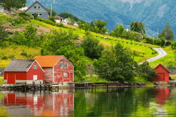 Drei norwegische rote Holzhäuser in Rosendal mit Bergen im Hintergrund und Wasser im Vordergrund