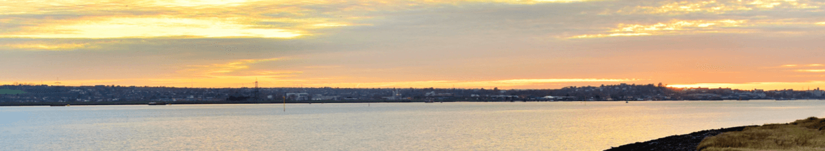 Tilbury in Essex gesehen aus der Perspektive der Themse bei Ebbe bei grauem Wetter mit dem steinigen Ufer im Vordergrund.