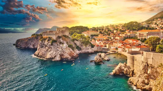 Die geschichtsträchtige Stadt Dubrovnik, fotografiert von ihrer Bucht aus, während eines spektakulären Sonnenuntergangs über den Dächern der Stadt.