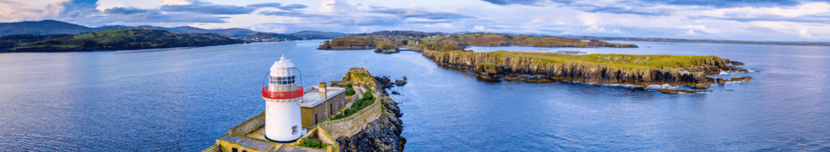 Luftaufnahmen des rot-weiß gestreiften Rotten Island Leuchtturms mit Killybegs und grünen Wiesen im Hintergrund, County Donegal, Irland.