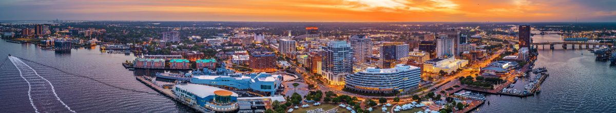Panorama-Luftaufnahme von Norfolk in Virginia mit dem Nauticus-Zentrum, der USS Wisconsin und dem Kreuzfahrthafen Half Moone Cruise Center am Elizabeth River bei Sonnenuntergang.