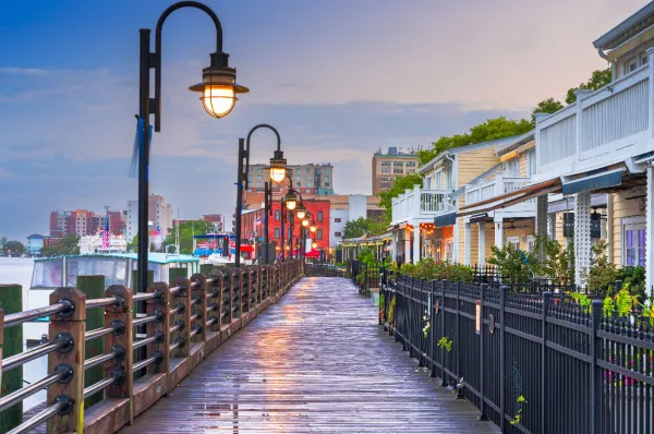 Hafen von Uferpromenade in Norfolk – Elizabeth River Trail bei Dämmerung Holzsteg der Uferpromenade in Norfolk bei Dämmerung mit beleuchteten historischen Laternen am Elizabeth River Trail für Landausflüge auf eigene Faust.