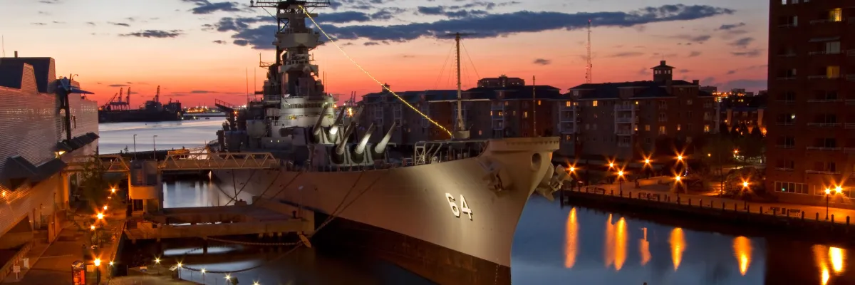Schlachtschiff USS Wisconsin (BB-64) in Norfolk bei Abenddämmerung Das historische Schlachtschiff USS Wisconsin (BB-64) im Abendlicht vor dem Nauticus-Museum in Norfolk mit stimmungsvollen Lichtreflexionen auf dem Elizabeth River.