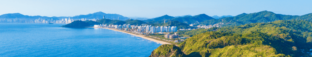 Luftbild von Itajaí mit Bergkette und hohen Gebäuden im Hintergrund und dem Südatlantik und einer begrünten Küste im Vordergrund, Santa Catarina, Brasilien