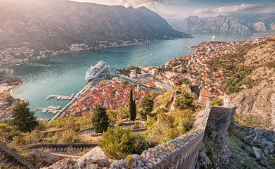 Panoramablick von der Festung San Giovanni auf die Altstadt von Kotor, die Bucht und ein im Hafen liegendes MSC Kreuzfahrtschiff bei Sonnenuntergang.