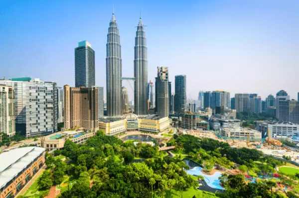 Sie dürfen bei keiner Sightseeing-Tour durch Kuala Lumpur fehlen: Die Petronas Towers sind die höchsten Zwillingstürme der Welt. Skyline von Kuala Lumpur mit den Petronas Towers, davor der KLCC Park mit Pool und vielen Bäumen.