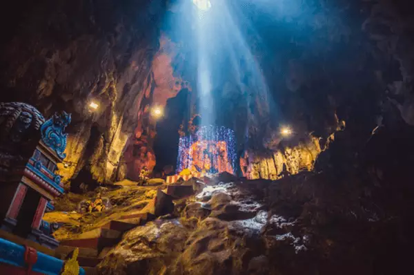 Durch die Decke fällt Licht auf einen Hindu-Schrein im Inneren der Batu Caves. Zusätzliche Scheinwerfer bringen die farbenfrohe Ausstattung noch mehr zur Geltung.