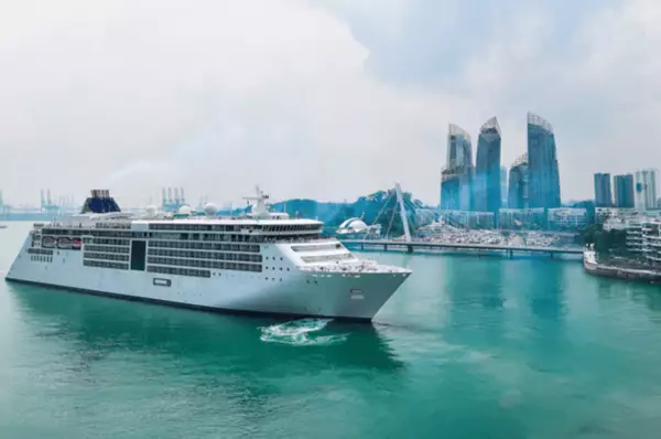 Ein luxuriöses Kreuzfahrtschiff im Hafen von Singapur, im Hintergrund sind einige Wolkenkratzer zu sehen.