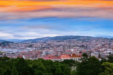 Vigo Skyline mit unzähligen Häuserdächern mit dem Berg und Hafen im Hintergrund bei Sonnenuntergang in Galicien, Spanien