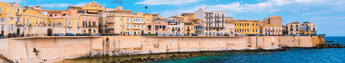 Küste von Ortigia in der Stadt Syrakus mit Häusern, die bis in das blaue Meerwasser hineinragen, Sizilien, Italien