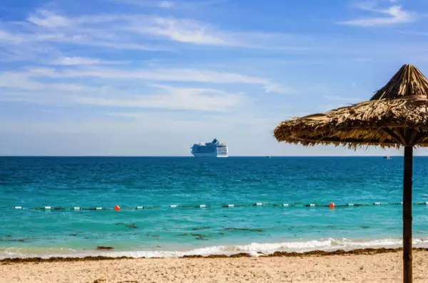 Kreuzfahrtschiff ankert auf dem türkisem Wasser mit Sandstrand im Vordergrund an der Insel Sir Bani Yas