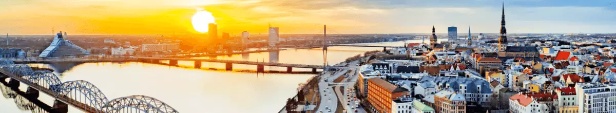 Panoramablick auf Riga, Lettland bei spätem Sonnenuntergang mit der alten Eisenbahnbrücke im Vordergrund.