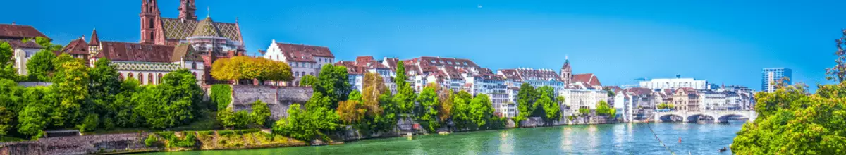 Das schöne Rheinufer in Basel mit dem Münster, den Häusern der Altstadt und einer Brücke mit drei Bögen.