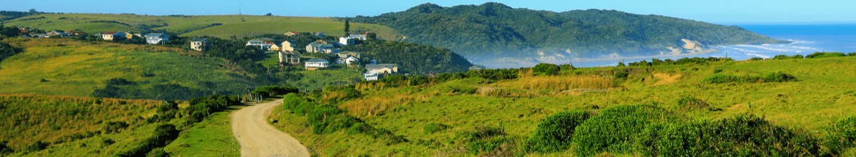 Schotterstraße auf grüner Wiese hinunter zum Strand von Morgans Bay mit tiefblauem Meer, East London Coast Nature Reserve, Provinz Ostkap, Südafrika